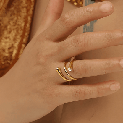 Bague tourbillon style atypique Thalissa en acier inoxydable plaqué or jaune 14K et cristal rond serti clos portée au doigt d'une femme vue de proche.