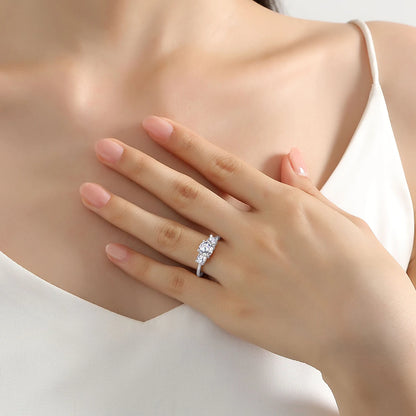 Bague trilogie en or blanc et diamants synthétiques portée au doigt d'une femme.