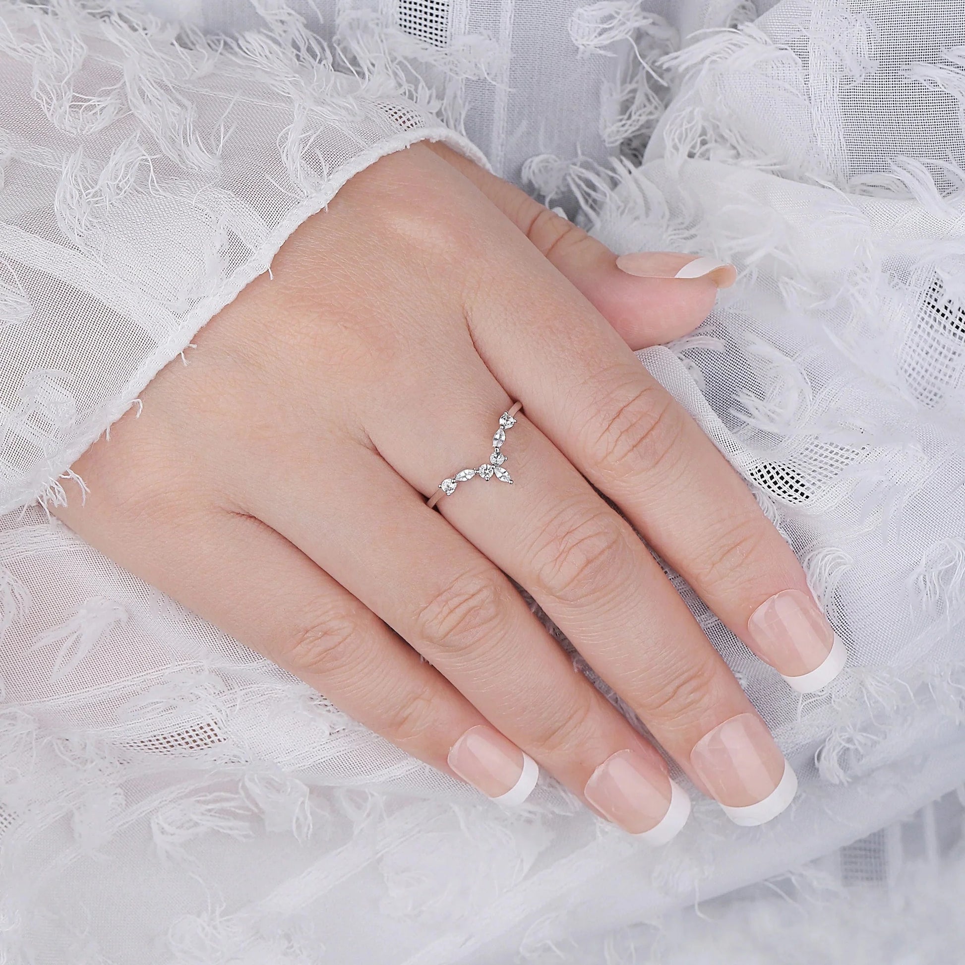 Bague V sept pierres en acier inoxydable plaqué or blanc et diamants étincelants portée au doigt d'une femme vue du dessus.
