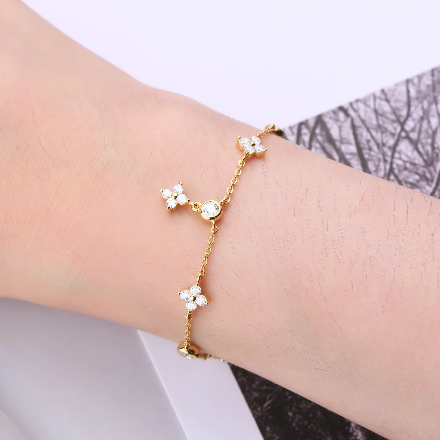Bracelet breloque fleur en argent sterling 925 plaqué or jaune et diamants porté au poignet d'une femme vue de proche.
