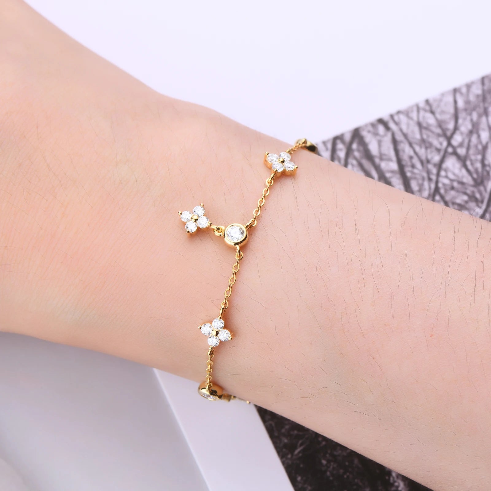 Bracelet breloque fleur en argent sterling 925 plaqué or jaune et diamants porté au poignet d'une femme vue de proche.