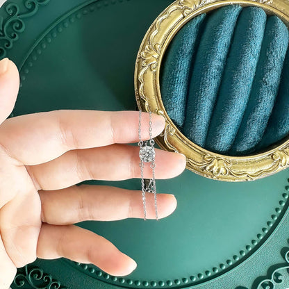 Bracelet chaîne double argentée en argent sterling 925 plaqué or blanc et moissanite solitaire sur les doigts d'une main de femme vue du dessus.