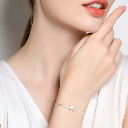 Bracelet chaîne double argentée en argent 925 plaqué or blanc et moissanite solitaire porté au poignet d'une femme vue de proche.