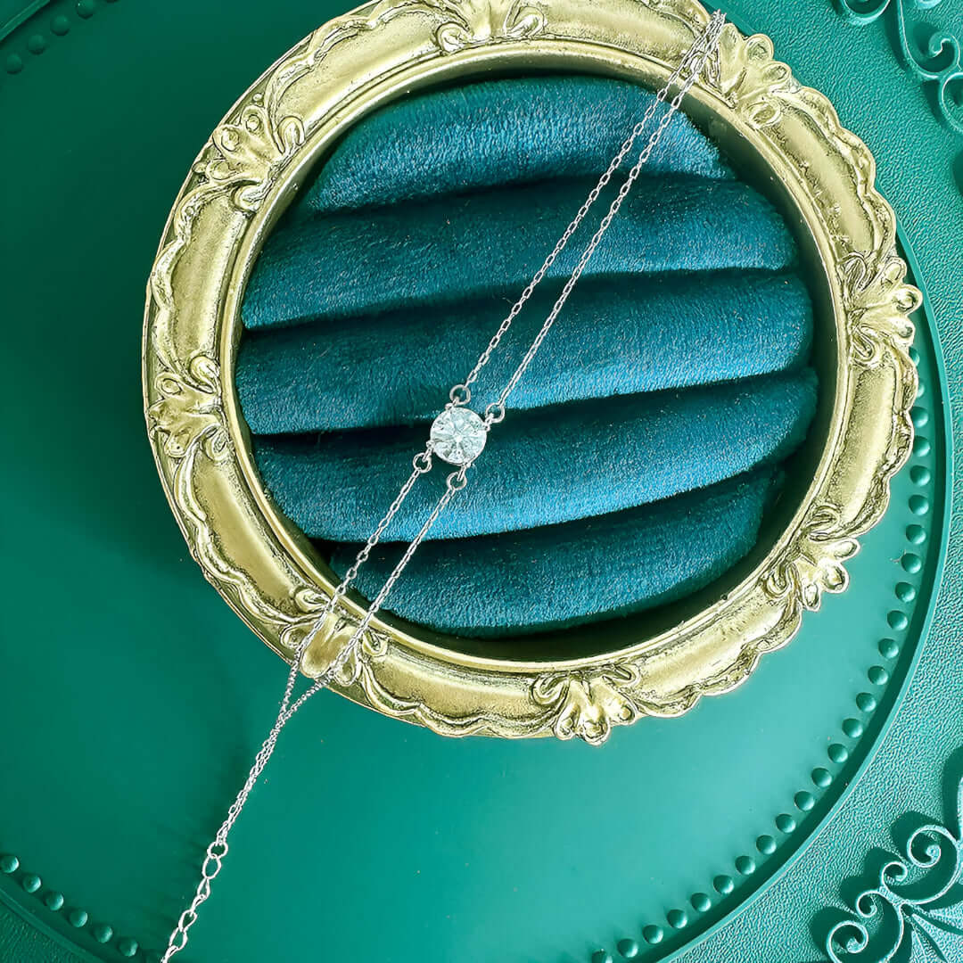 Bracelet chaîne double argentée en argent 925 plaqué or blanc délicat et moissanite solitaire à plat sur un socle.