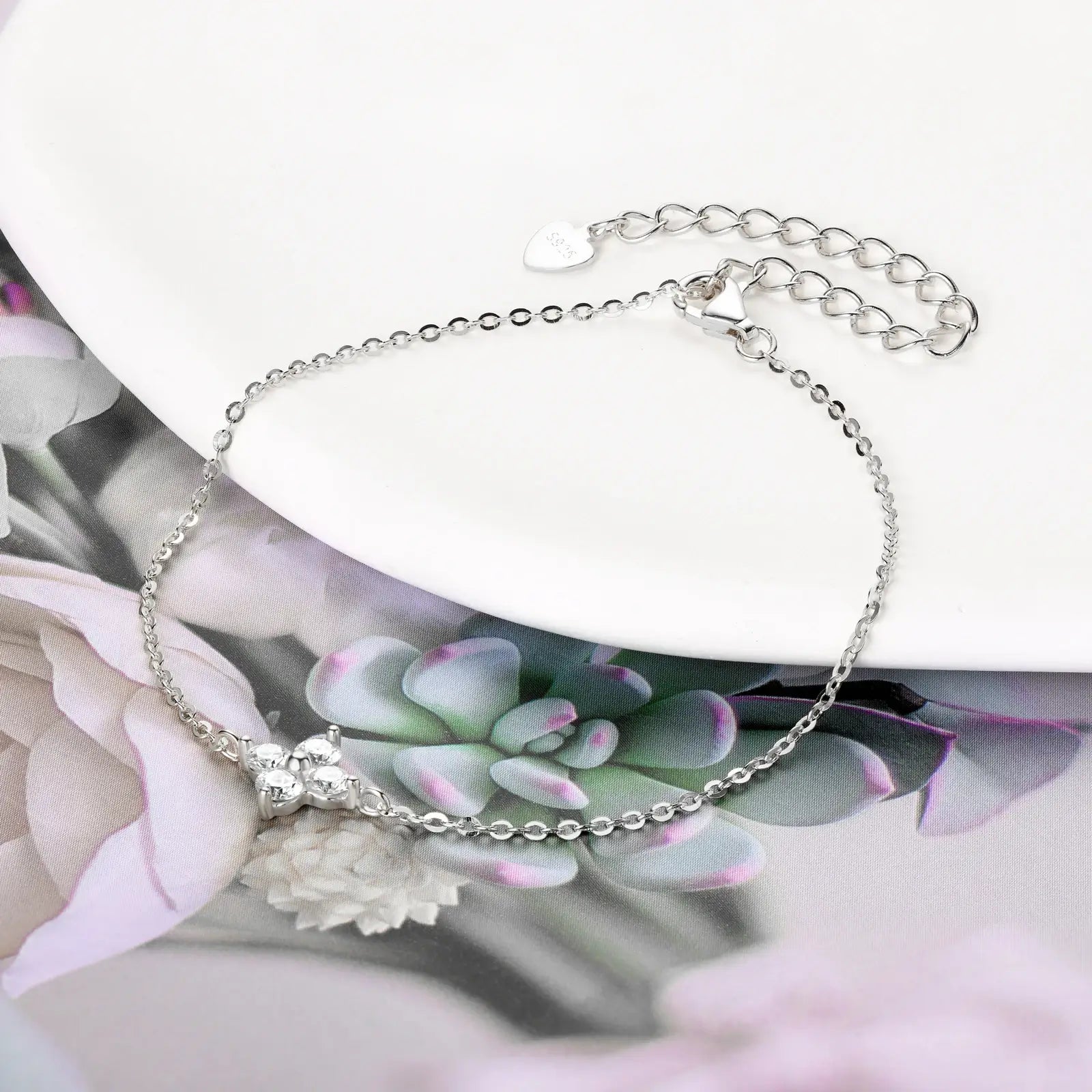 Bracelet chaîne fine fleur pavée en argent 925 plaqué or blanc délicat et moissanites à plat sur une surface blanche.