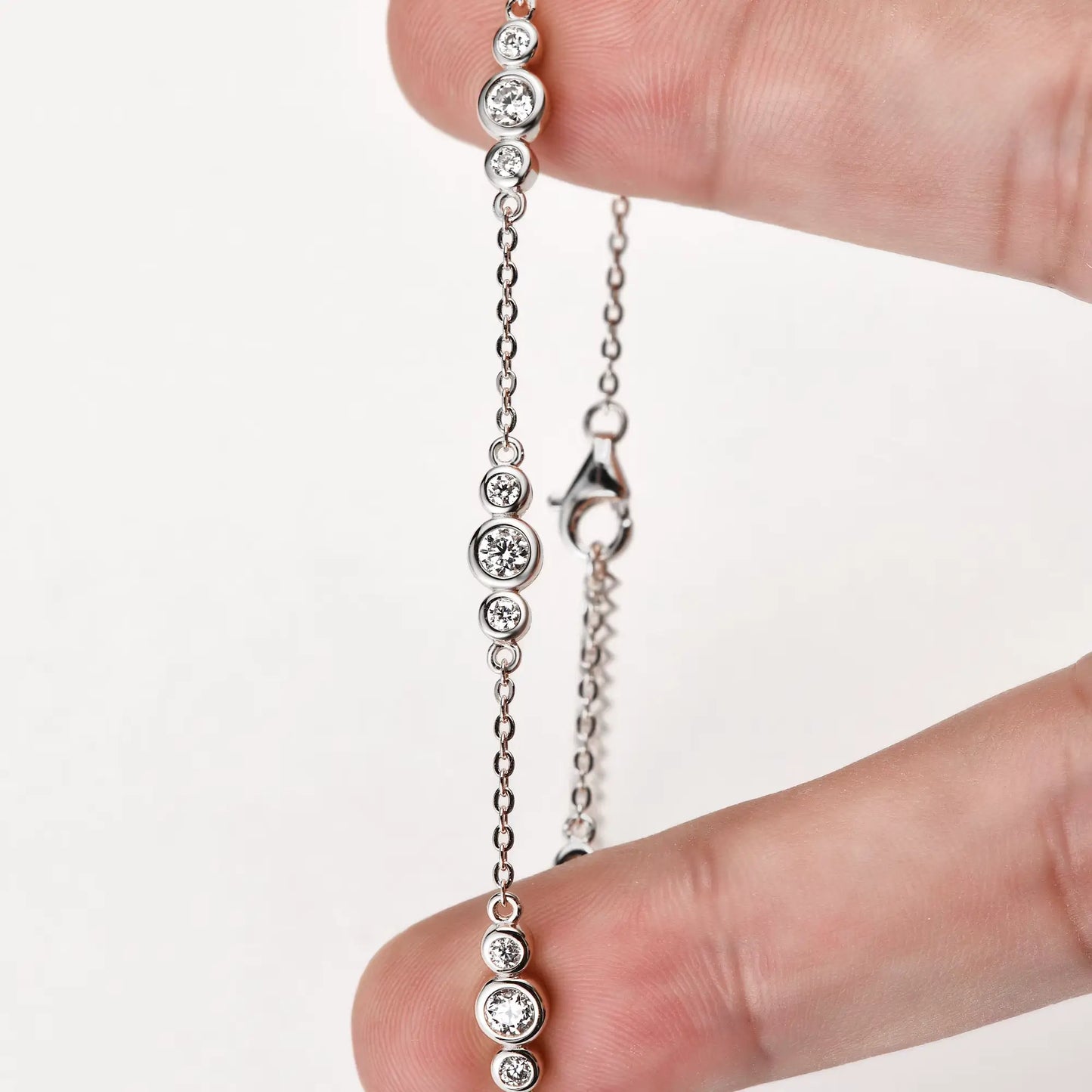 Bracelet chaîne sinueuse trio de pierres en argent 925 plaqué or blanc et moissanites entre les doigts d'une main vue de proche.