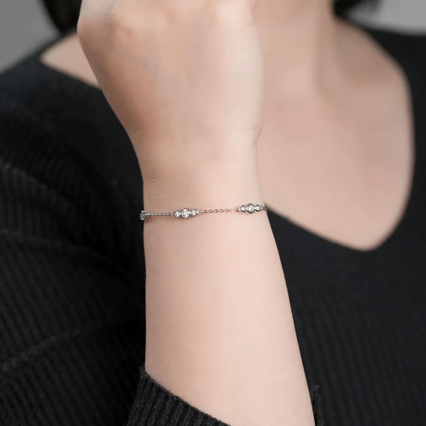 Bracelet chaîne sinueuse trio de pierres en argent 925 plaqué or blanc et moissanites scintillantes porté au poignet d'une femme vue de face.