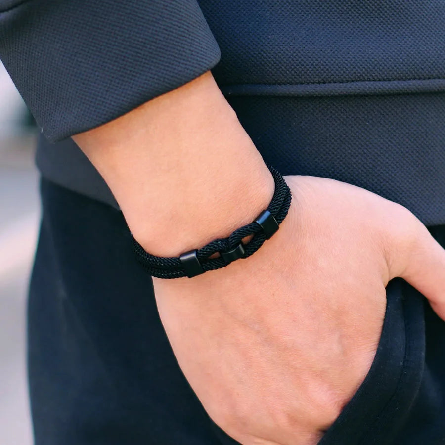 Bracelet double cordon noir fermoir loquet pivotant porté au poignet d'un homme.