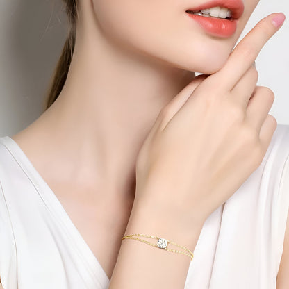 Bracelet double maile dorée en argent 925 plaqué or jaune et diamant solitaire scintillant porté au poignet d'une femme vue de proche.