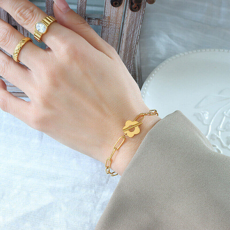 Bracelet fleur en acier plaqué or jaune porté au poignet d'une femme.