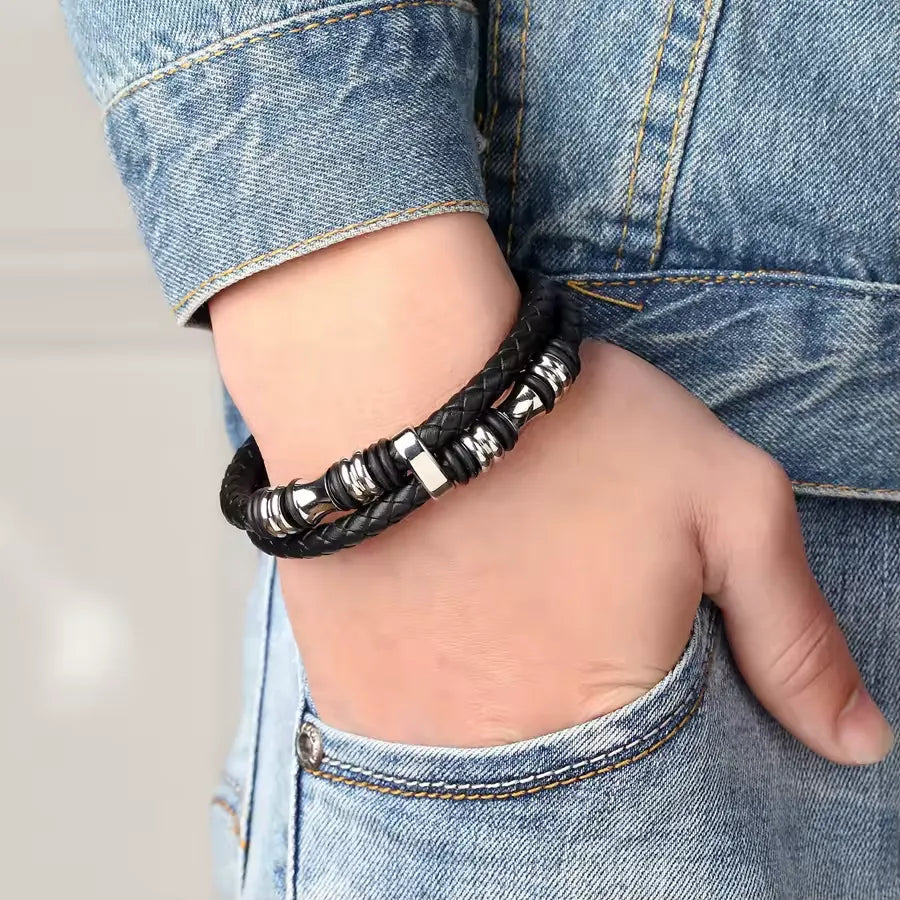 Bracelet homme en cuir tressé noir et acier inoxydable plaqué titane blanc porté au poignet d'un homme.