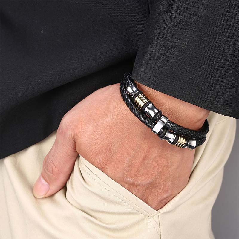 Bracelet homme en cuir tressé noir et acier inoxydable plaqué or jaune porté au poignet d'un homme.