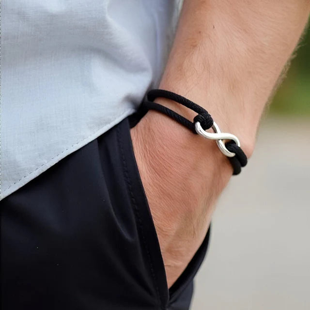 Bracelet infini ajustable en acier inoxydable blanc et cordon noir porté au poignet d'un homme vue de proche.