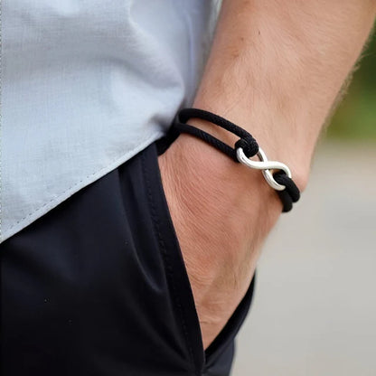 Bracelet infini ajustable en acier inoxydable blanc et cordon noir porté au poignet d'un homme vue de proche.