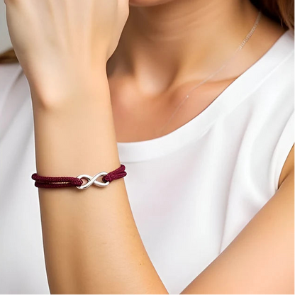 Bracelet infini ajustable en acier inoxydable blanc et cordon rouge bordeaux porté au poignet d'une femme.