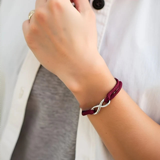 Bracelet infini ajustable en acier inoxydable blanc et cordon rouge bordeaux porté au poignet d'une femme vue de proche.