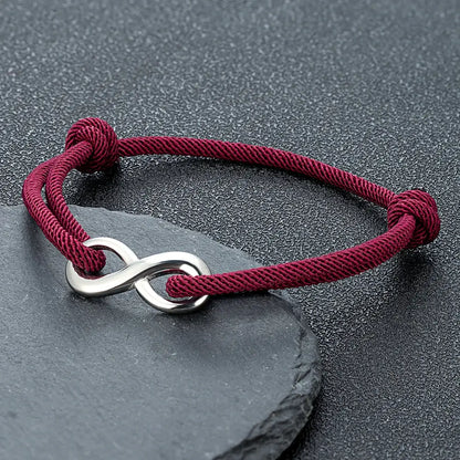 Bracelet infini ajustable en acier inoxydable blanc et cordon rouge bordeaux posé.