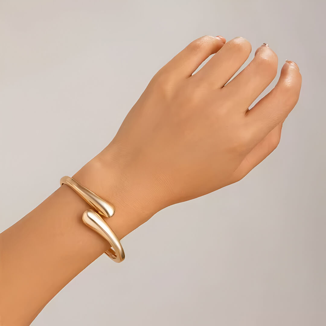 Bracelet jonc goutte d'eau en or jaune porté au poignet d'une femme.