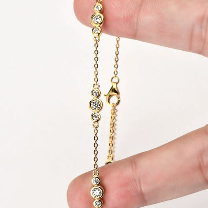 Bracelet maille fluide triple pierres en argent 925 plaqué or jaune et diamants étincelants entre les doigts d'une femme vue de face.