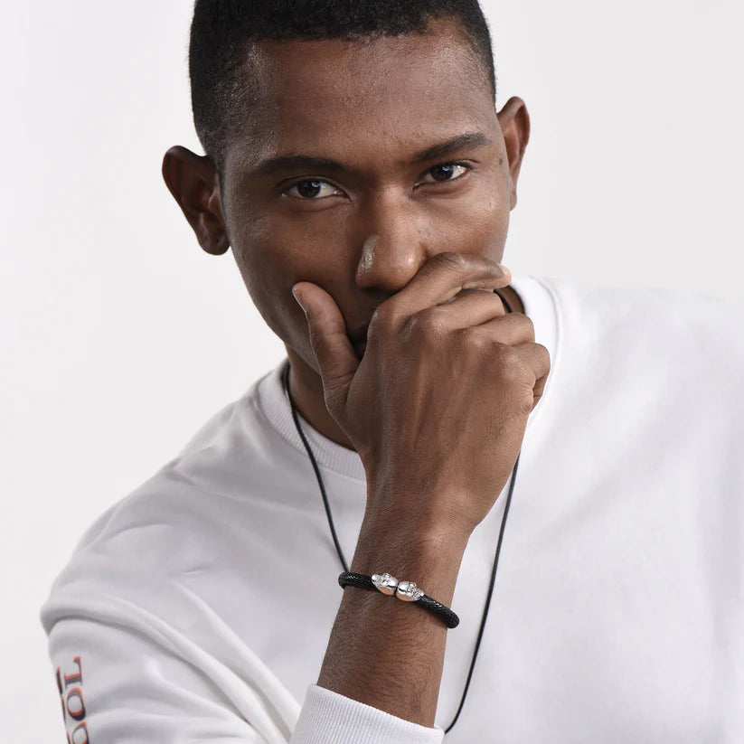 Bracelet tête de mort en cuir tressé noir et acier inoxydable plaqué titane blanc porté au poignet d'un homme.