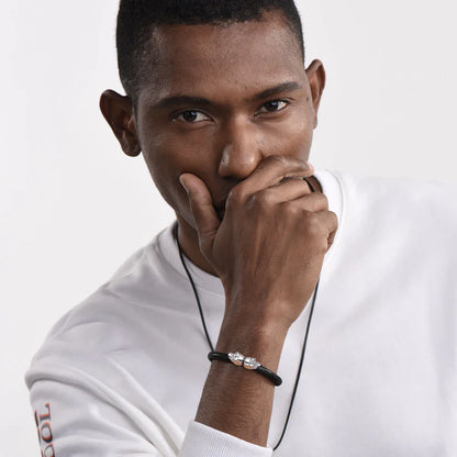 Bracelet tête de mort en cuir tressé noir et acier inoxydable plaqué titane blanc porté au poignet d'un homme.