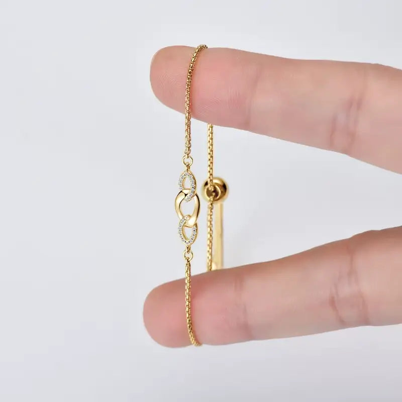 Chaîne amovible nœud en argent plaqué or jaune et diamants synthétiques entre les doigts d'une femme.