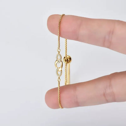 Chaîne amovible nœud en argent plaqué or jaune et diamants synthétiques entre les doigts d'une femme.