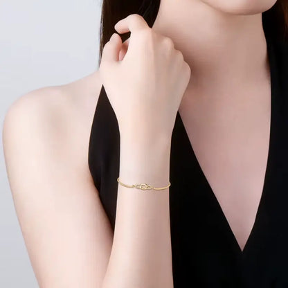 Chaîne amovible nœud en argent plaqué or jaune et diamants synthétiques portée au poignet d'une femme vue de face.