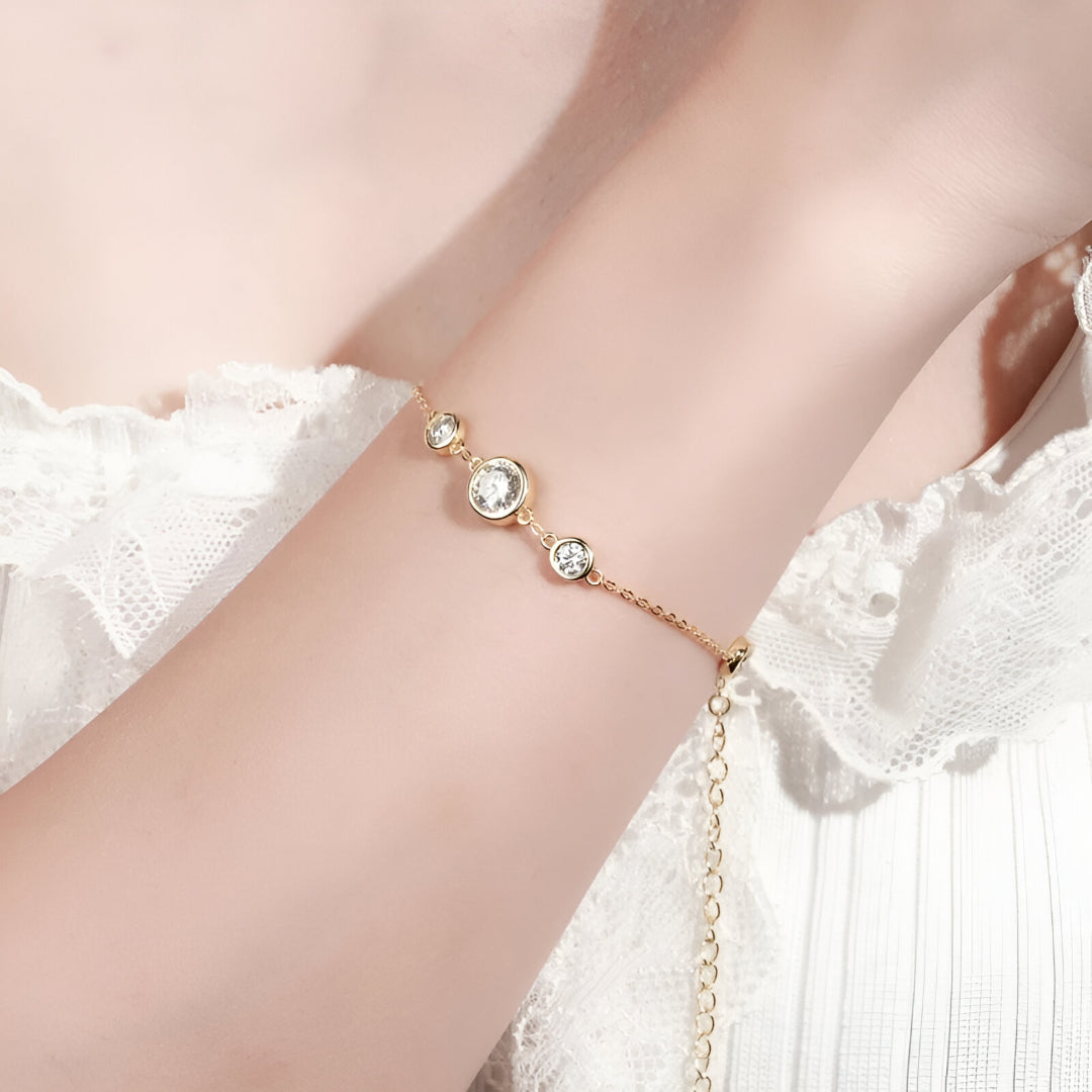 Chaîne cinq pierre en or jaune et diamants synthétiques portée au poignet d'une femme.