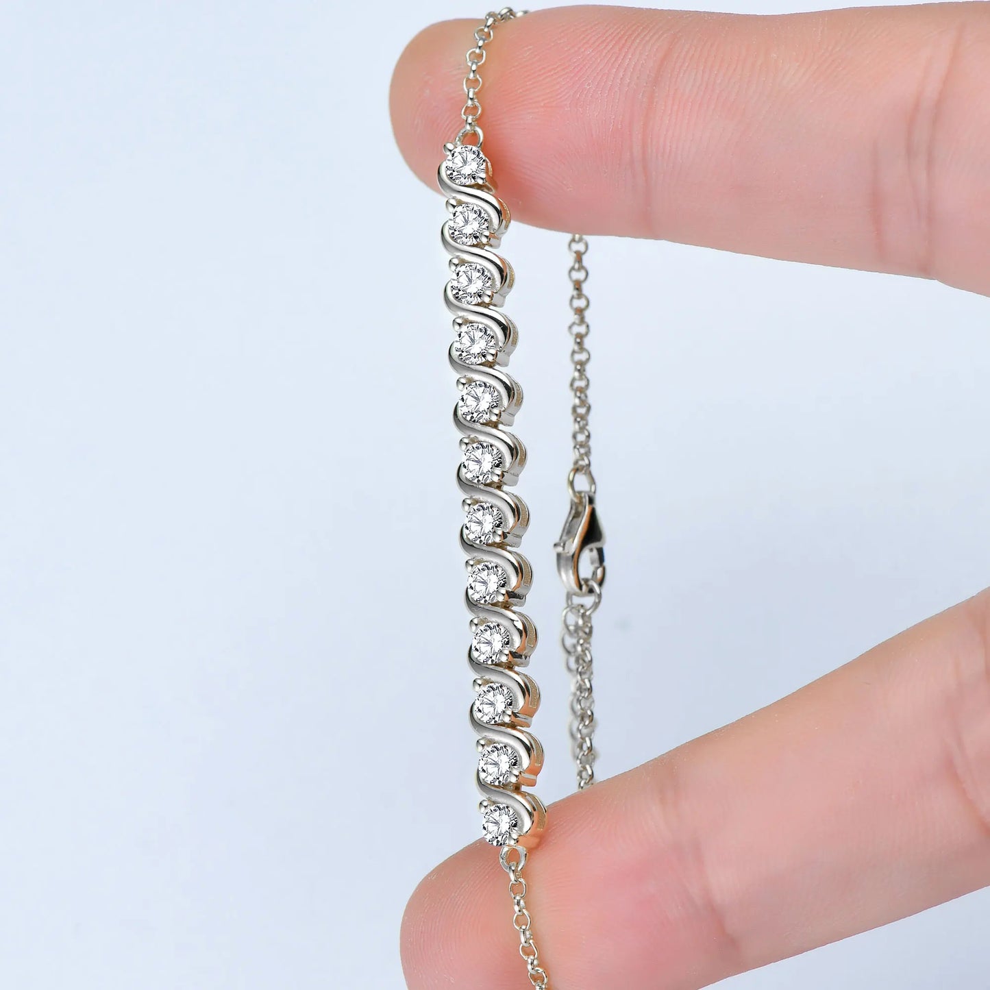 Bracelet Chaîne fluide en argent 925 plaqué or blanc et diamants en moissanite entre les doigts d'une femme.