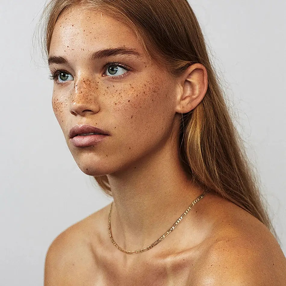 Chaîne maille figaro en argent sterling plaqué or jaune portée au cou d'une femme.