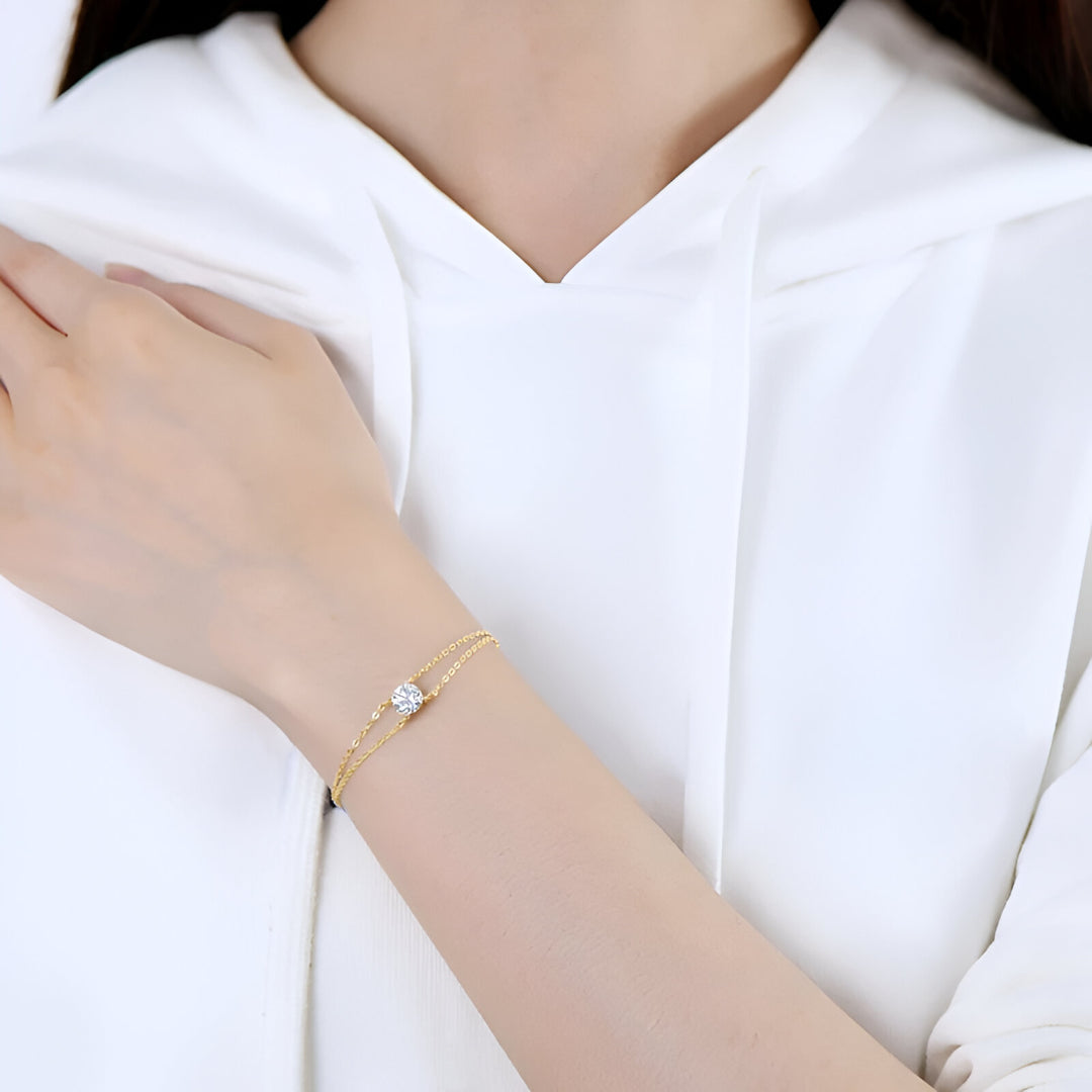 Chaîne solitaire en or jaune et diamant synthétique portée au poignet d'une femme vue de face.