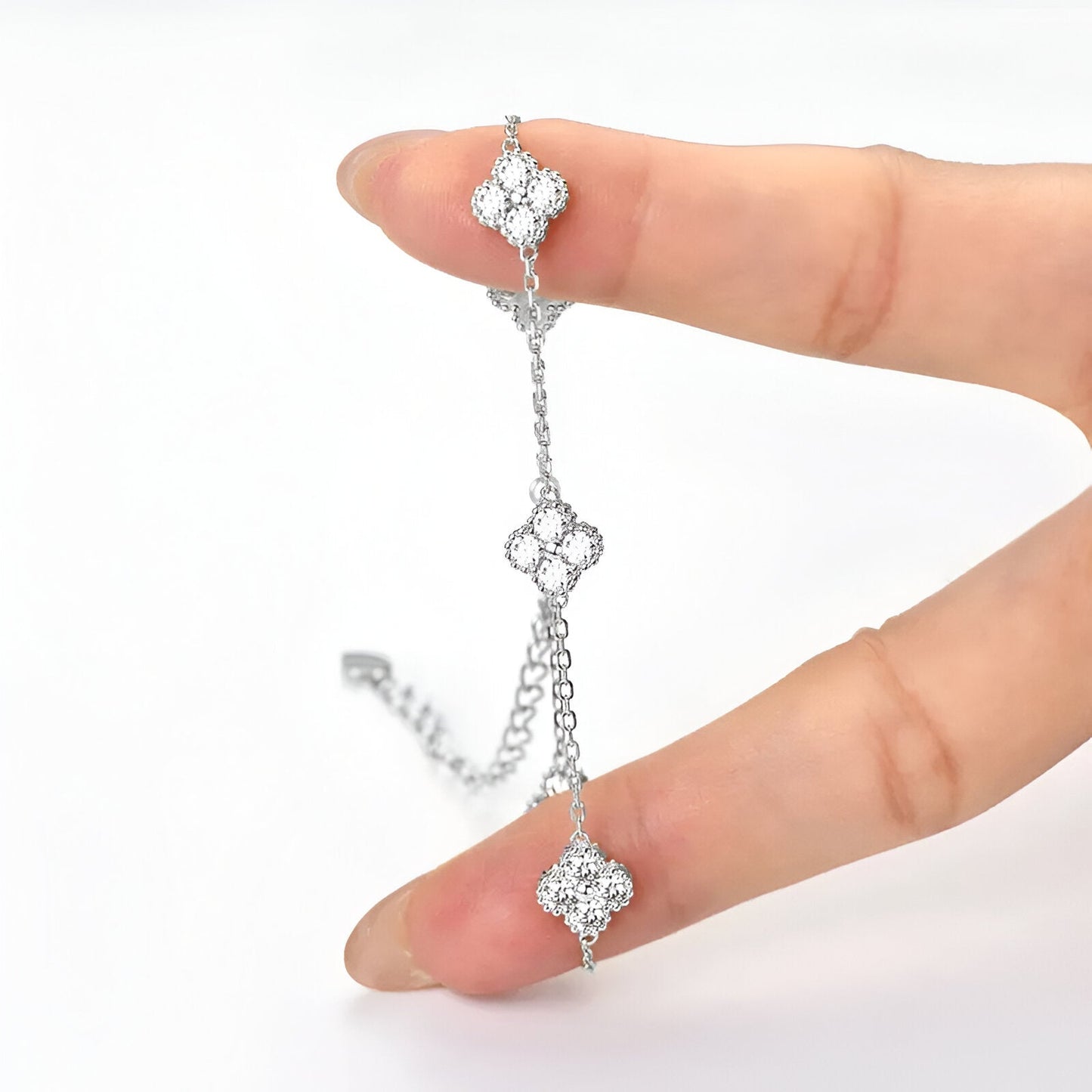 Chaîne trèfle à quatre feuilles en or blanc et diamants synthétiques sur une main vue de face.