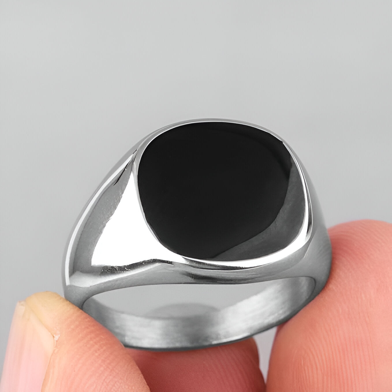 Chevalière moderne unisexe Nyx en acier plaqué or blanc 18K délicat et onyx de forme elliptique montrée entre les doigts d'une femme vue de proche.