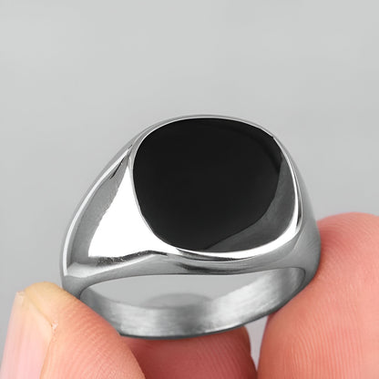 Chevalière moderne unisexe Nyx en acier plaqué or blanc 18K délicat et onyx de forme elliptique montrée entre les doigts d'une femme vue de proche.