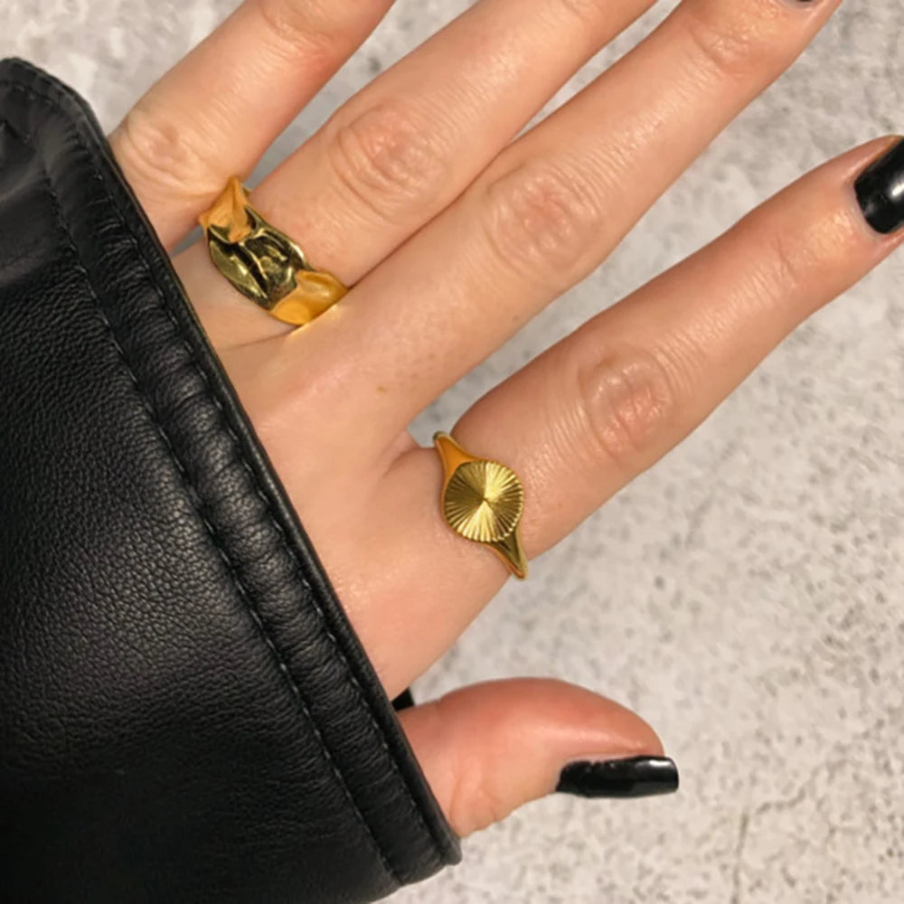 Chevalière pavé arrondi rainuré en acier plaqué or jaune portée au doigt d'une femme vue du dessus.