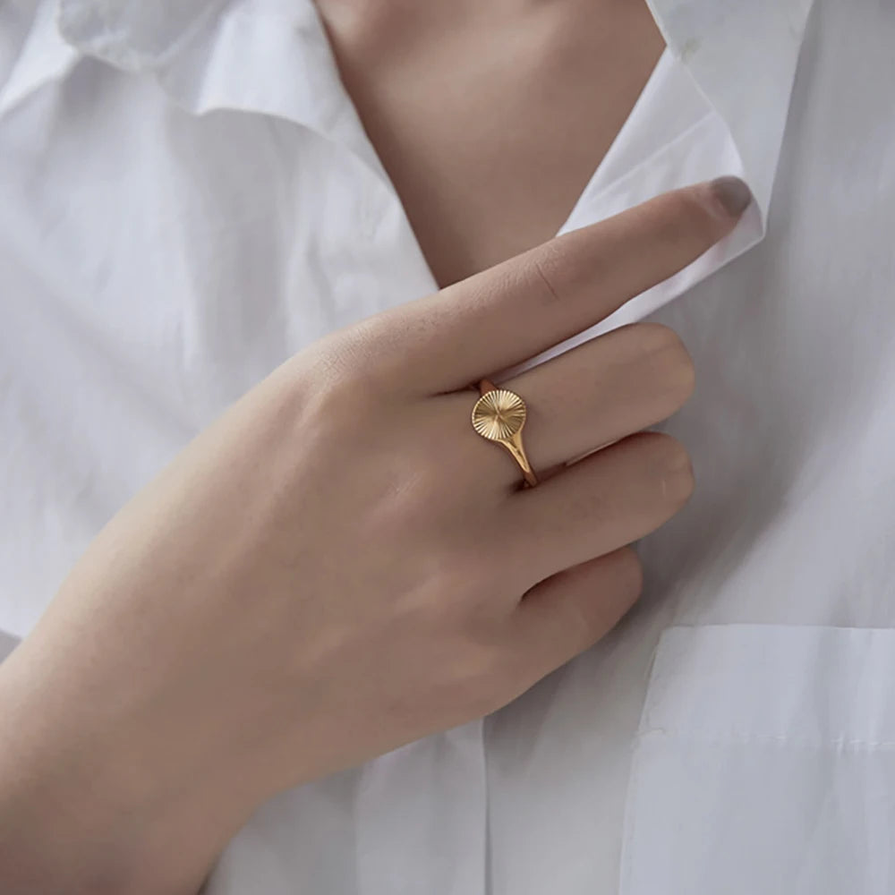 Chevalière pavé arrondi rainuré en acier plaqué or jaune portée au doigt d'une femme vue de face.