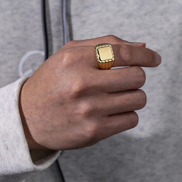 Chevalière pavé rainuré en acier doré portée au doigt d'un homme.