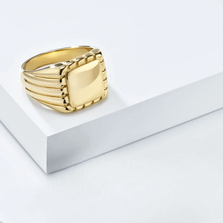 Chevalière pavé rainuré en acier doré à plat.