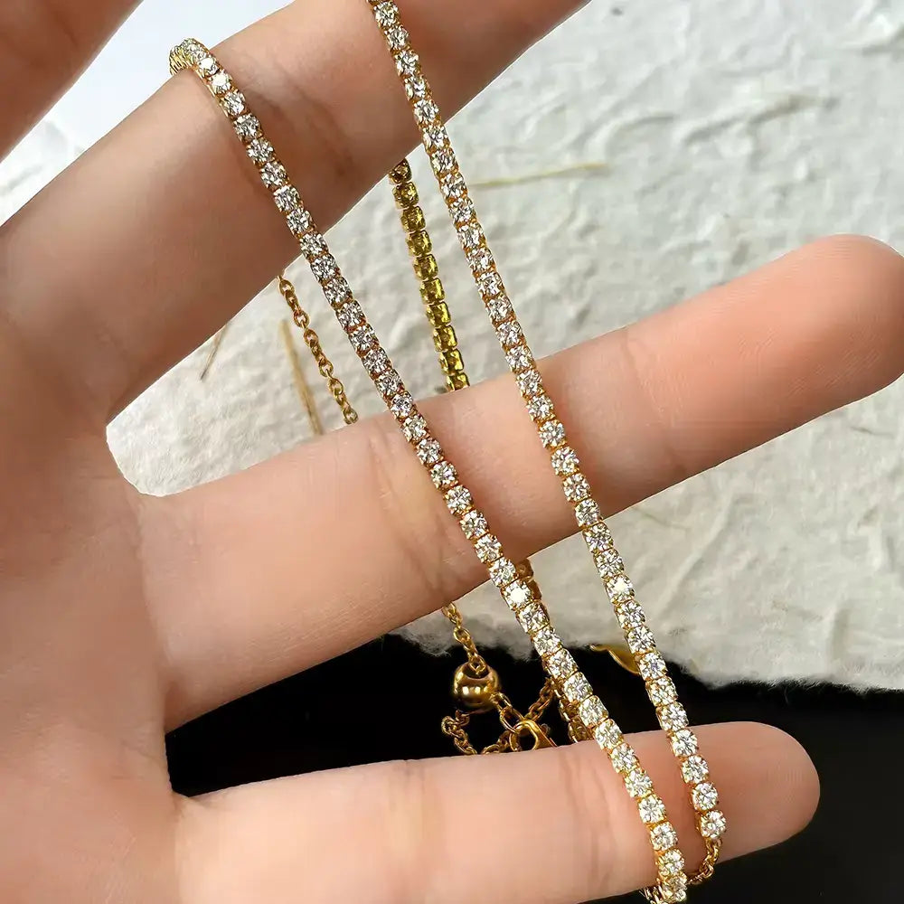 Collier chaîne courte pavé en argent 925 plaqué or jaune et diamants étincelants entre les doigts d'une femme vue de proche.