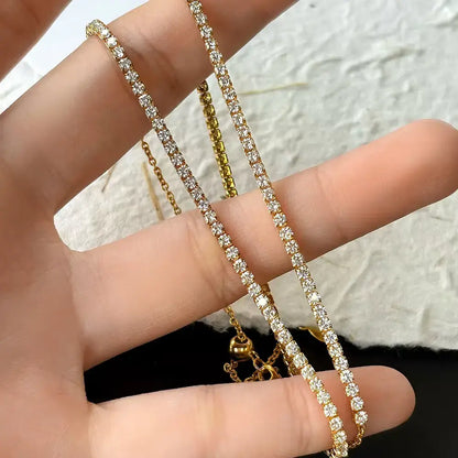 Collier chaîne courte pavé en argent 925 plaqué or jaune et diamants étincelants entre les doigts d'une femme vue de proche.
