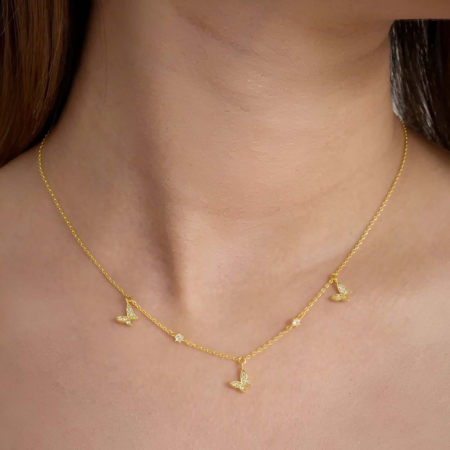 Collier chaîne dorée papillons en argent 925 plaqué or jaune et diamants porté au cou d'une femme vue de proche.
