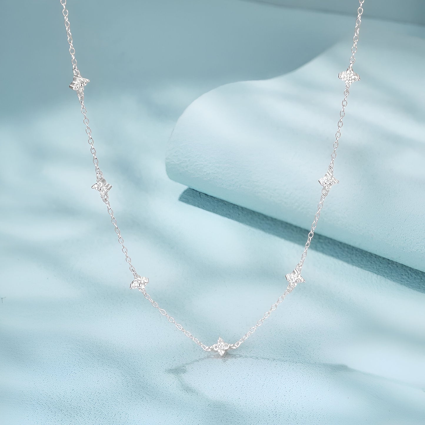 Détail du pendentif étoilé du Collier Constellation en argent 925 et or blanc 18k avec moissanite éclatante sur fond bleu – zoom chaîne or blanc