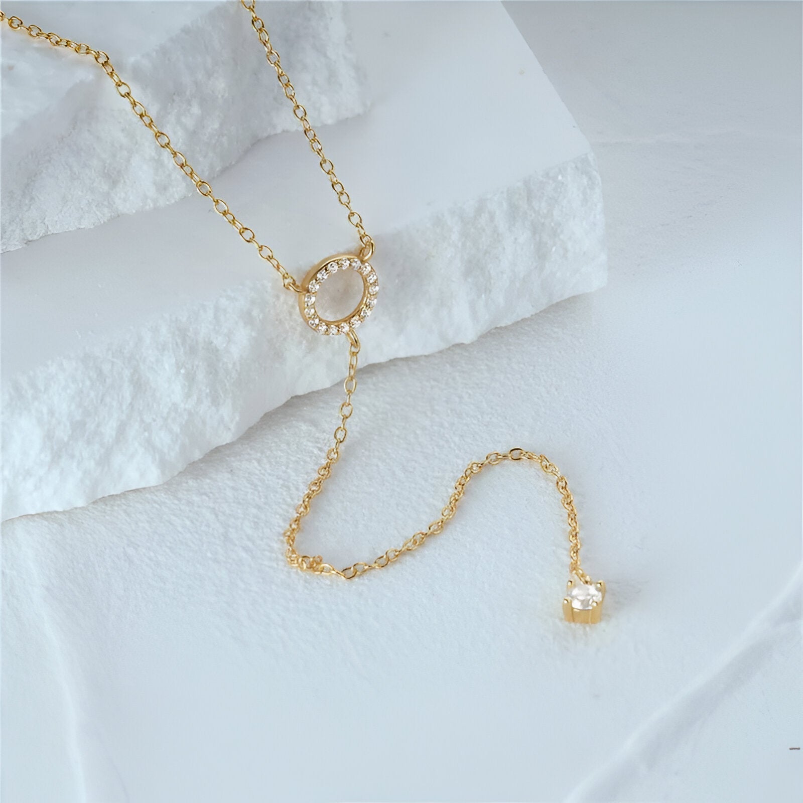 Collier lariat Miravelle en argent 925 plaqué or jaune et diamants scintillants posé sur une roche blanche.