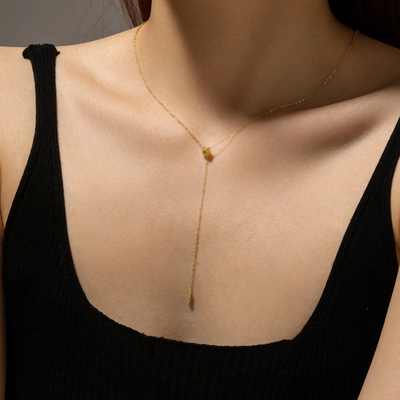 Collier long pendentif rectangulaire en argent 925 plaqué or jaune et diamants vert et blancs porté au cou d'une femme.
