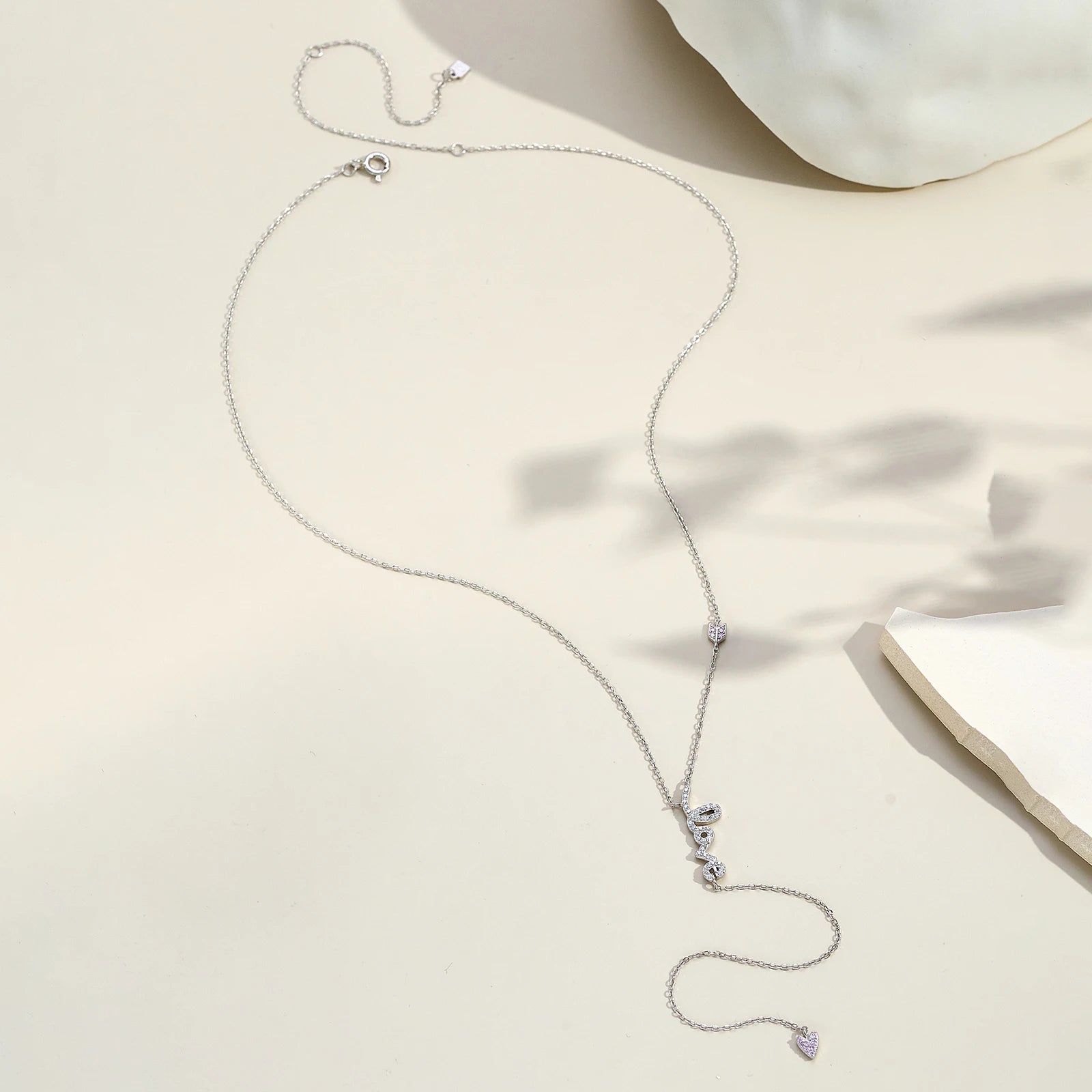 Collier love long pendentif cœur en argent 925 plaqué or blanc et diamants en zircon blancs et roses à plat vue en entier.