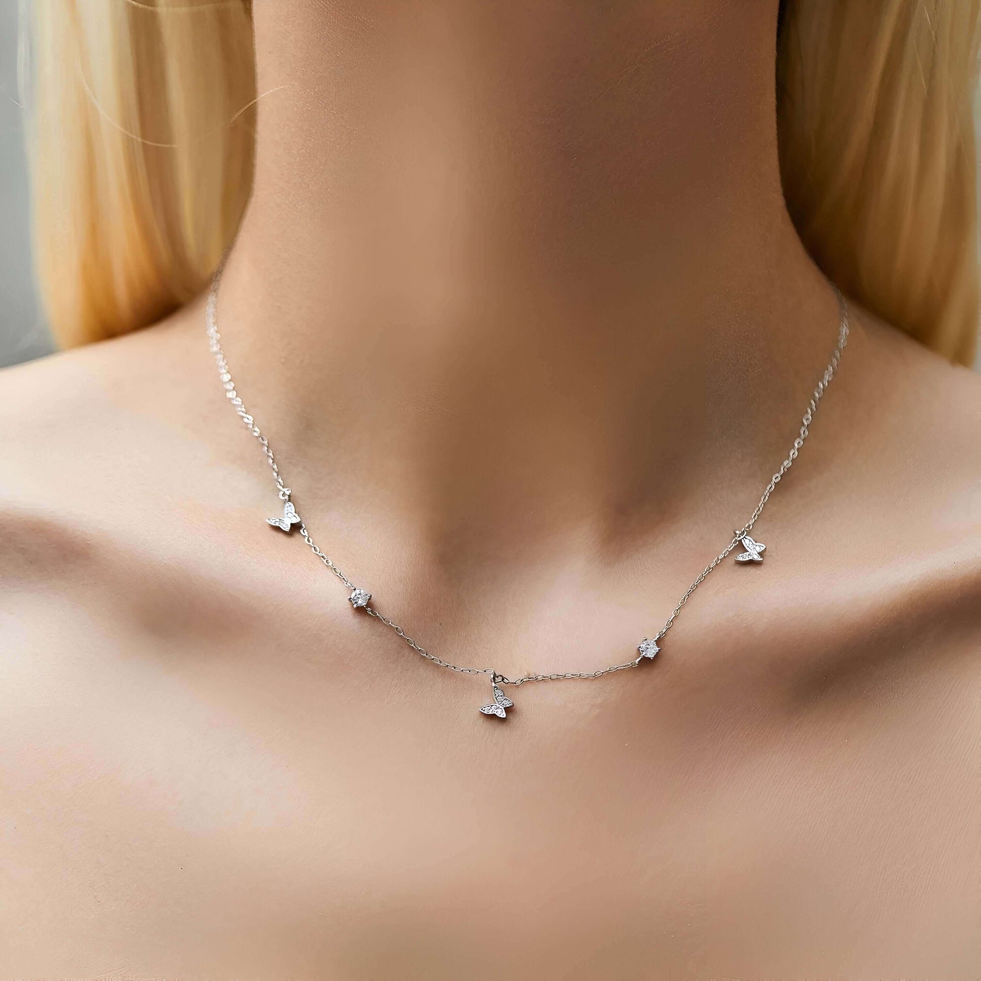 Collier maille argentée papillons en argent 925 plaqué or blanc et zircons scintillants porté au cou d'une femme vue de face.