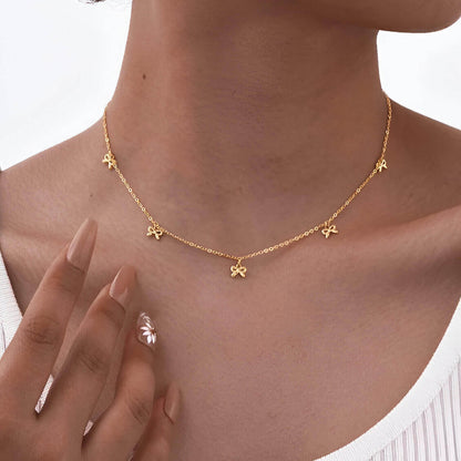 Collier nœud papillon en acier inoxydable plaqué or jaune variante breloques porté au cou d'une femme.