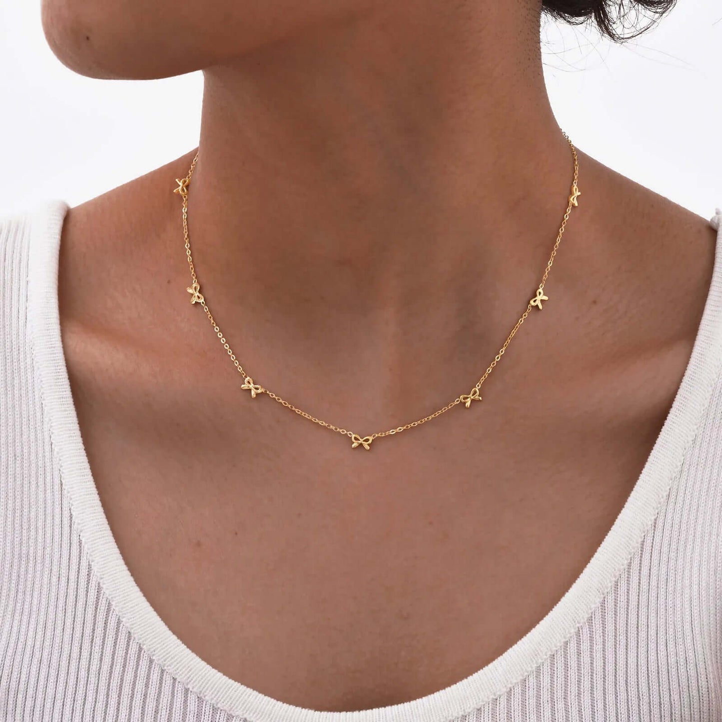 Collier nœud papillon en acier inoxydable plaqué or jaune variante incrusté porté au cou d'une femme.