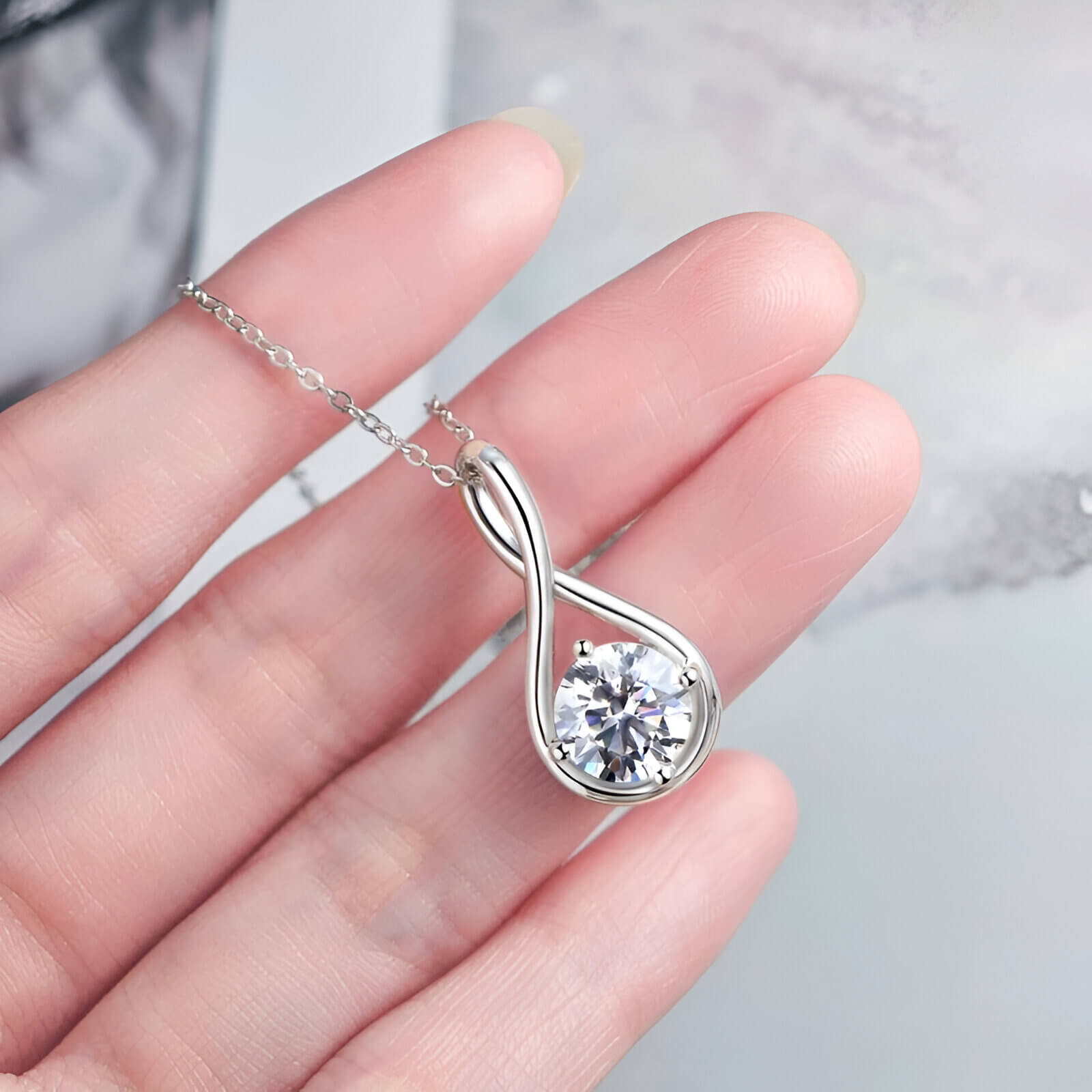 Pendentif goutte arqué en argent 925 plaqué or blanc discret et moissanite solitaire sertie 4 griffes sur une main vue de proche.